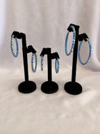 Aurora Collection Blue Zircon AB skinny hoop earrings for ballroom dance featuring iridescent teal Austrian crystals on a black display stand.