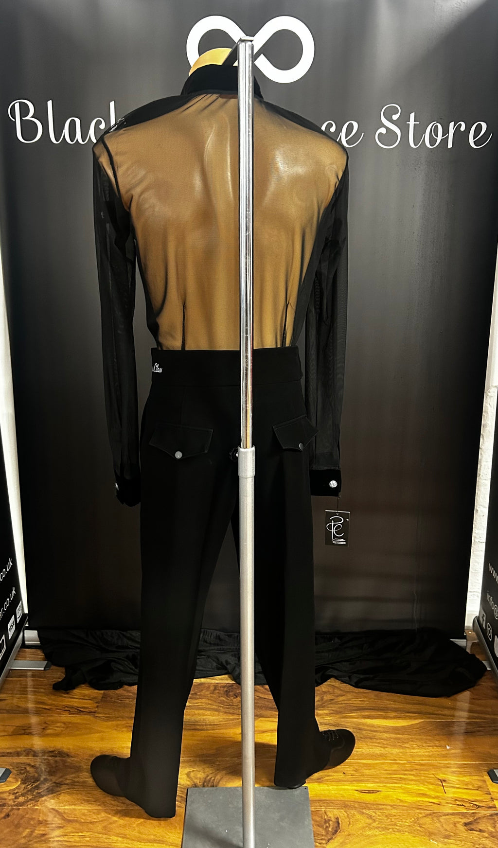 Back view of the Pure Class Mark Shirt on a mannequin highlighting the translucent sheer black mesh back panel and the clean fit over high waisted Latin trousers.