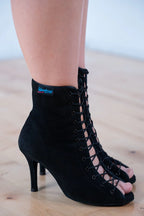 Close-up side view of a dancer wearing the open-toe Hannah black suede lace-up dance boot by International Dance Shoes on a clean wooden studio floor.