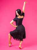 Woman in a black dress with a fringed skirt posing against a pink background