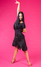 Woman in a black dress with fringe posing against a pink background