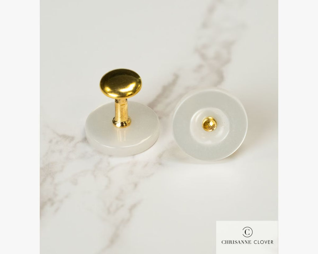 A pair of gold Chrisanne Clover collar studs showing the specialized curved front fastening mechanism and flat back base resting on a white marble surface.