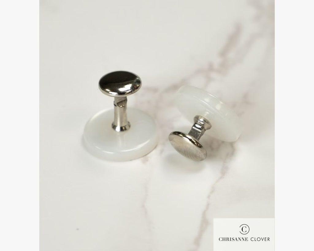 A pair of silver Chrisanne Clover collar studs showing the specialized curved front fastening mechanism and flat back base resting on a white marble surface.