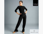 Full-length studio shot of a dancer posing in the black Chrisanne Clover Eternity Top paired with wide-leg practice trousers and gold ballroom practice shoes.