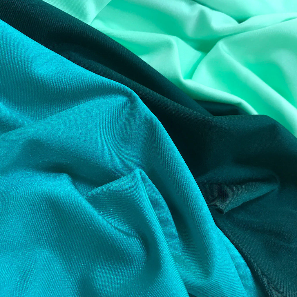 Draped display of Chrisanne Clover Lustre Lycra in shades of Mint and Teal, highlighting the fabric's luxurious high-shine finish and performance stretch.